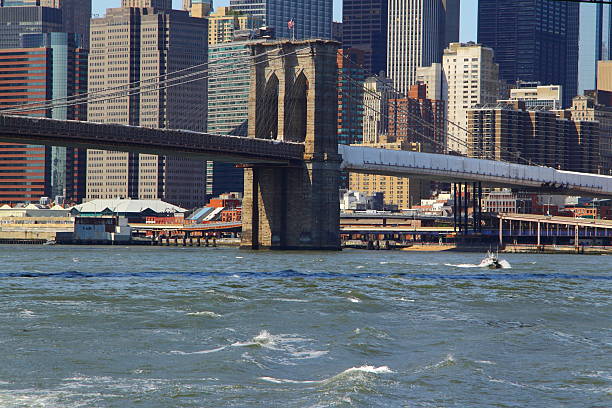 A detailed view of the stone masonry of the Brooklyn Bridge tower with the dense architectural backdrop of Lower Manhattan.