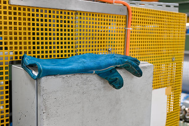 Close-up of a blue safety work glove positioned against a yellow panel inside a factory, highlighting industrial work environments, safety equipment, and contrasting colors in manufacturing settings.