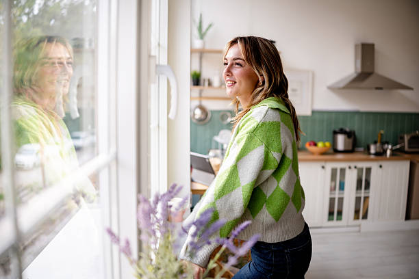 istock Young woman enjoying time in a bright kitchen while looking out the window with a smile 2253406855