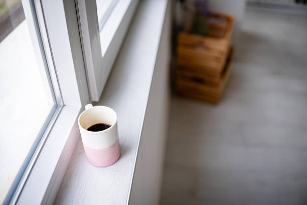 A young woman smiles as she sits in her kitchen, holding a cup of coffee. Sunlight fills the space, highlighting the simple joys of morning routines at home.
