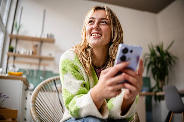 istock Young woman enjoys time in the kitchen while using her phone and smiling happily 2253411800