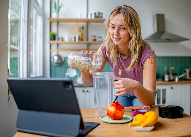 istock Young woman prepares a healthy smoothie at home while enjoying a cooking tutorial in the kitchen 2253413092