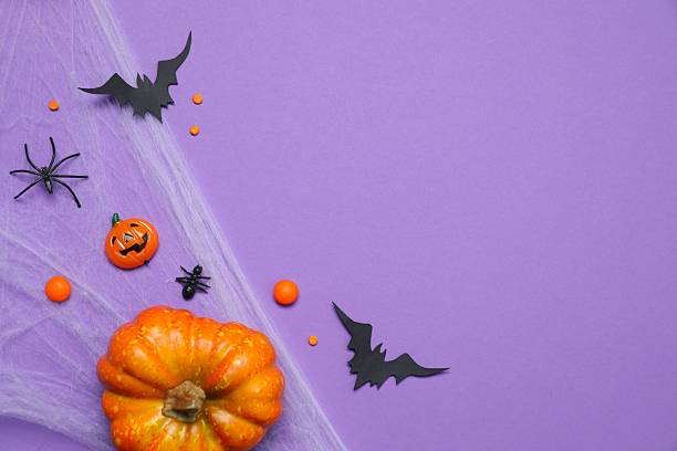 istock Halloween holiday decorations including cobweb, pumpkins, bats and spiders on purple background, top view 2253414721