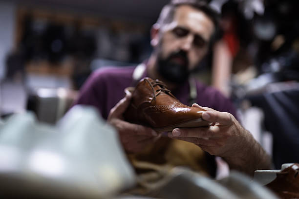 Craftsman holds a brown leather shoe in a workshop while inspecting its details
