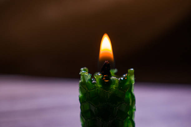 Three white candles are burning, casting a warm, flickering light in a dark setting. The flames are bright orange and yellow, standing out against the black background. Melted wax drips down, forming pools at the base of the candles. The glossy surface beneath reflects the candle flames, enhancing the moody and intimate atmosphere. The scene evokes a sense of calm and simplicity.