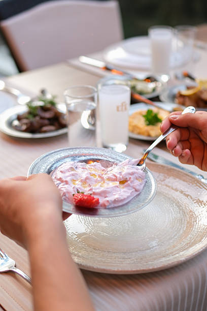 A group of friends sharing traditional Turkish meze dishes at a restaurant table. Close-up view of hands serving and tasting appetizers such as salads and cold starters, creating a warm and social dining atmosphere. Concept of friendship, Mediterranean cuisine, and social eating.