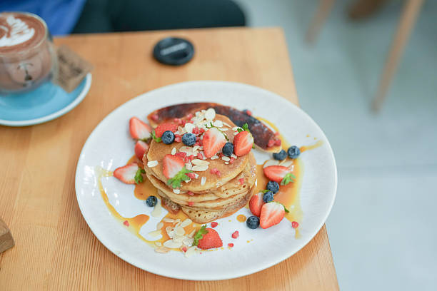 A stack of pancakes with strawberries and blueberries on top. The plate is on a wooden table