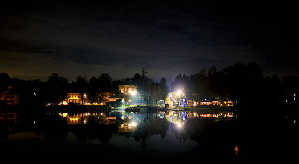 City lights glowing at night and reflected on calm river water, creating a symmetrical and atmospheric urban landscape. Quiet waterfront scene with dark sky and luminous reflections, suitable for concepts such as calm, reflection, balance, night atmosphere, serenity, and slow urban life.