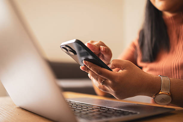 istock Woman using smartphone while working on a modern laptop at a desk 2253431386
