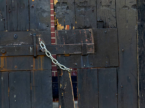 Rusty chains and a padlock are used to secure a wooden gate, showcasing weathered textures and a sense of confinement in a natural environment.