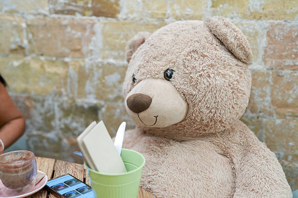 A teddy bear is sitting on a table with a book and a cup