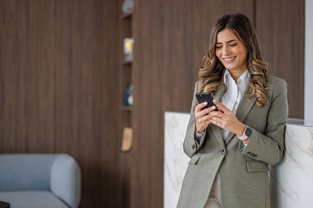 istock Professional businesswoman smiling while using smartphone in modern office building lobby, checking messages 2253437763
