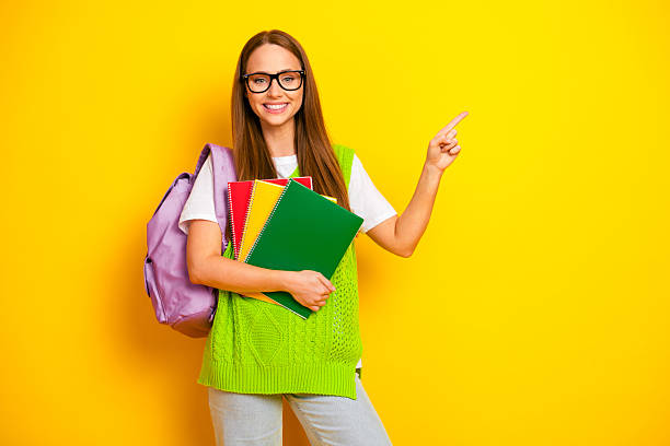 istock Young student with glasses smiles and points to notebooks against a bright yellow background 2253439774