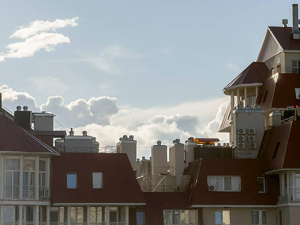 Clouds gather above rooftops with various designs and features during the afternoon hours.