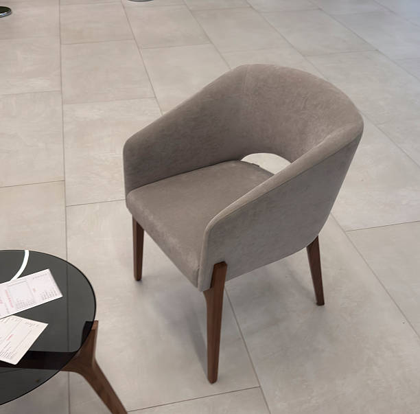 A chair stands alone by a table in a bright indoor space. Papers are on the table beside it.