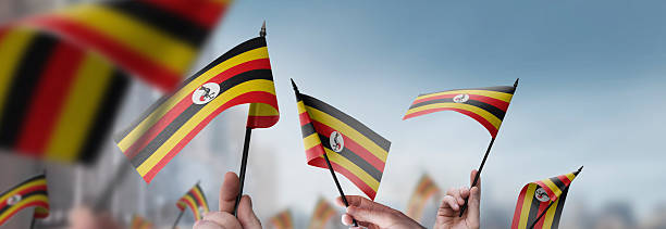 Uganda flags in their hands on a blurred urban background. The photo illustration was created without the use of artificial intelligence, only using Photoshop.
