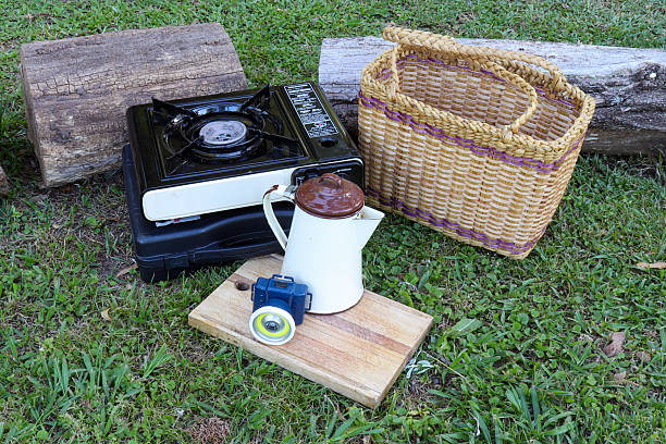 Picnic cooking set with portable gas stove wicker basket enamel kettle and wooden board on grass. Outdoor life and camping gear accessories