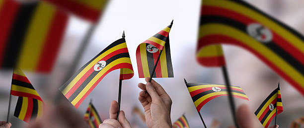 Uganda flags in their hands on a blurred urban background. The photo illustration was created without the use of artificial intelligence, only using Photoshop.
