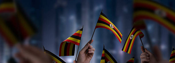 Uganda flags in their hands on a blurred urban background. The photo illustration was created without the use of artificial intelligence, only using Photoshop.