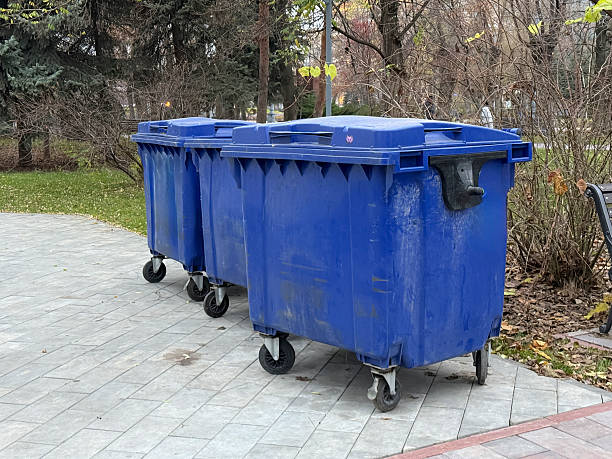istock Blue trash bins are on a stone path in a park surrounded by grass and trees 2253441519