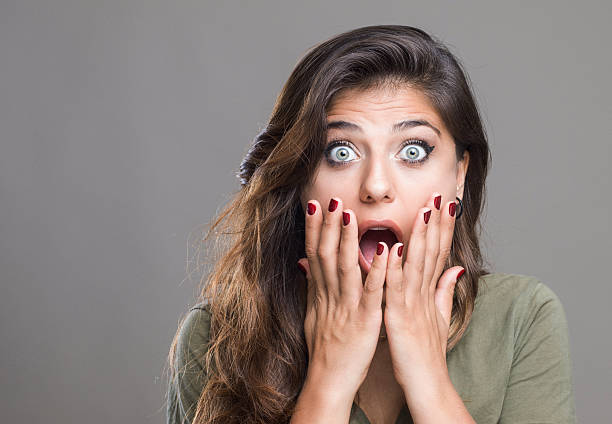 Young woman with wide eyes and open mouth expressing shock and surprise. Studio portrait with hands on face, dramatic facial expression