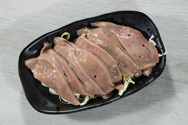 Fresh raw pork liver slices arranged on a black plate with shredded cabbage garnish.