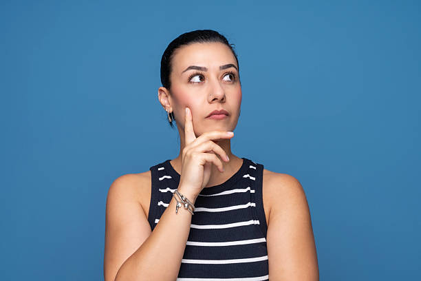 A young woman with a thoughtful expression looking upward while touching her chin.