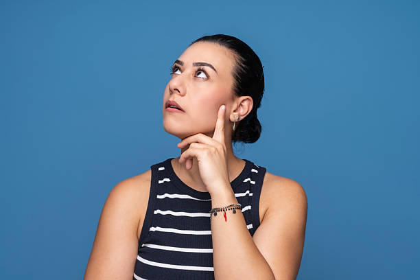 A young woman with a thoughtful expression looking upward while touching her chin.