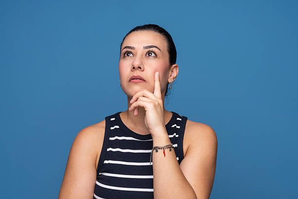 A young woman with a thoughtful expression looking upward while touching her chin.