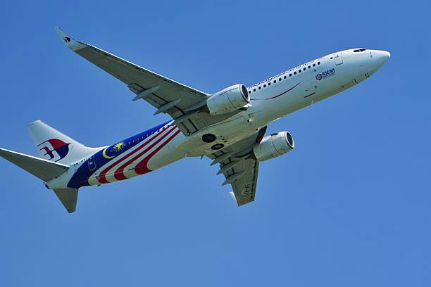 Kedah, Malaysia, December 3, 2025: Malaysia Airlines Boeing 737 featuring Malaysian flag livery soars through a clear blue sky, showcasing national pride and modern aviation against scenic clouds.