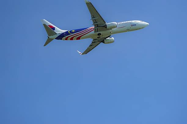 Kedah, Malaysia, December 3, 2025: Malaysia Airlines Boeing 737 featuring Malaysian flag livery soars through a clear blue sky, showcasing national pride and modern aviation against scenic clouds.