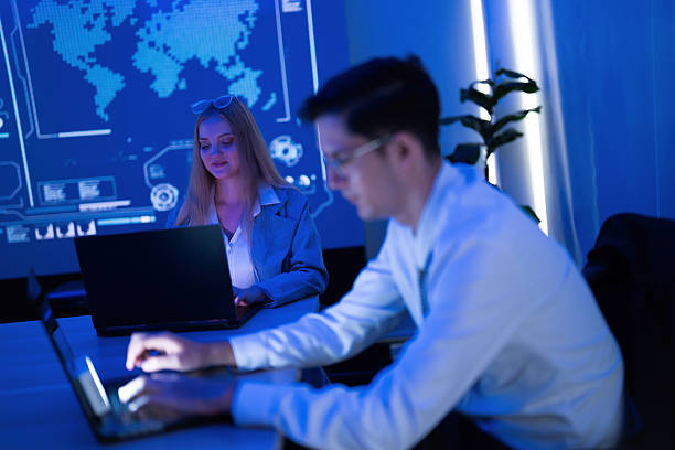 istock Two professionals collaborating on laptops in a modern workspace with a digital world map in the background at night 2253448138