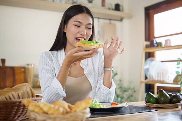 Young woman enjoying a healthy avocado toast for breakfast at home in a cozy kitchen.