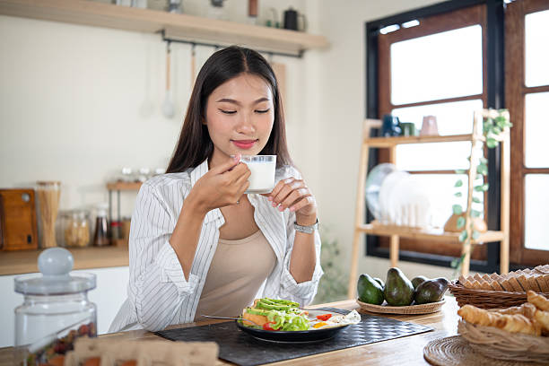 Young woman holding a glass of milk while enjoying a healthy breakfast at home kitchen.