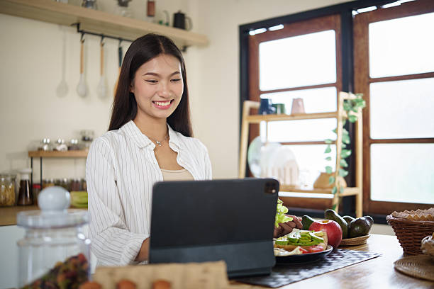 Beautiful Asian woman enjoying morning routine, working on digital tablet with fresh meal on wooden table.