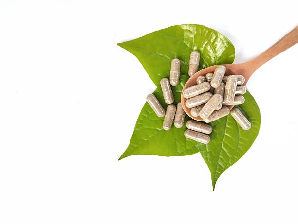 istock Herbal capsules in wooden spoon with fresh herb leaf on white background. 2253451453