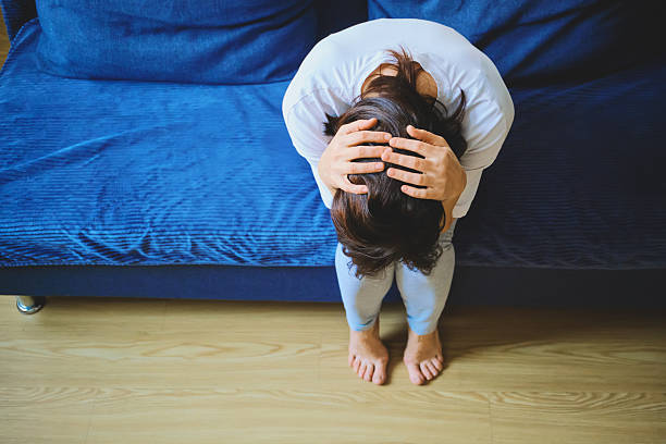 istock Woman sitting on sofa with hands on her head, experiencing headache, mental health problems 2253456627