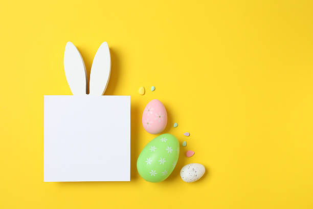 istock Happy Easter. Colorful eggs, bunny ears nd white paper card on a pastel color background, space for text or advertising 2253459130