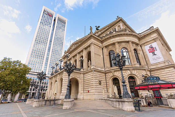 Frankfurt, Germany - October 21, 2025: Wide angle perspective of the Old Opera House building, set against a sleek, modern skyscraper under a blue sky on a sunny autumn day in Frankfurt.
