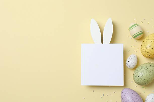 istock Happy Easter. Colorful eggs with bunny ears and paper card on color background, space for text or advertising 2253459808