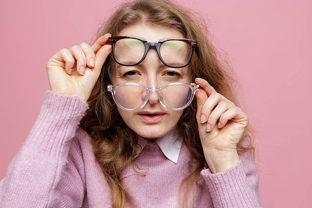 istock Woman comparing two eyeglass frames choosing new glasses on pink background 2253459815