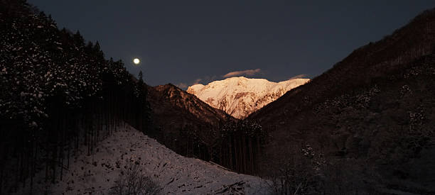 Cold Moon setting over snowy Mt. Tanigawa before dawn. Ethereal winter landscape in Gunma, Japan.