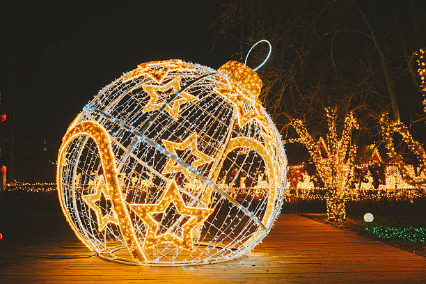 istock Large golden glowing festive ornament with star patterns illuminating a dark night path and decorated trees. 2253461225