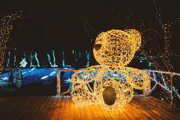 Illuminated bear sculpture sits on wooden deck surrounded by sparkling blue festive lights at night.