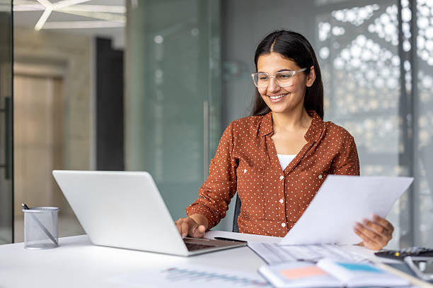 istock Indian businesswoman working on laptop holding documents smiling 2253462384
