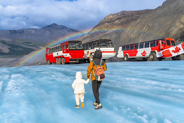 Mother and child walking on athabasca glacier with special buses and a rainbow in the background, located in jasper national park, a popular tourist destination in the canadian rockies