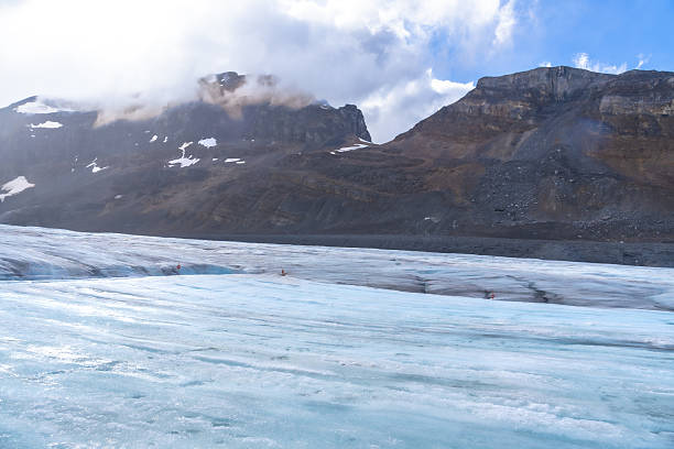 Tourists are walking on the surface of the athabasca glacier, part of the columbia icefield in jasper national park, alberta, canada, on a sunny, cloudy day