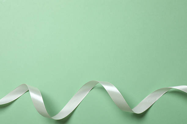 Beautiful white silk ribbon on green background, space for text