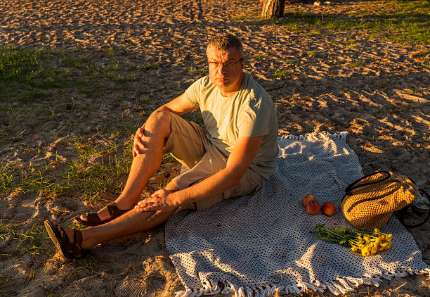 Adult man in white tank top and jeans taking rest under olive tree in summer