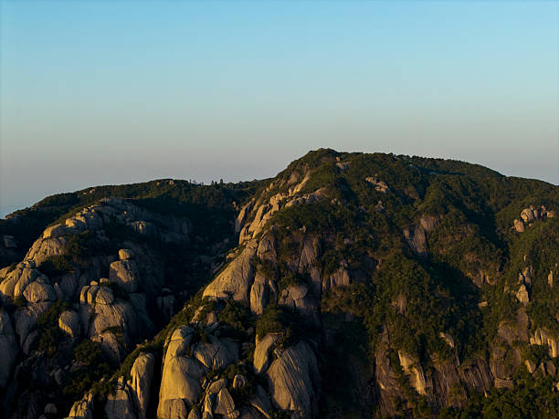 This aerial photograph captures a mountainous landscape during dusk, showcasing rugged terrain and dense forests. The visual style is naturalistic, emphasizing the serene beauty of the wilderness. It has high potential for use in nature documentaries or travel brochures.